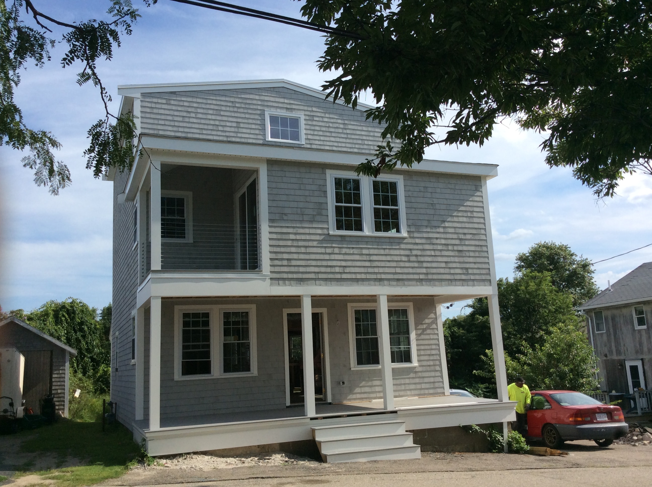 After photo — front view of the transformed home completed by Boston J's featuring an expanded upper level, covered front porch with columns, upper balcony and shingle-style exterior