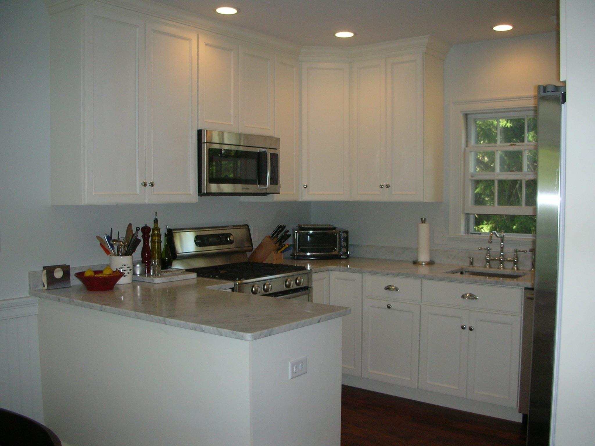 After photo of a remodeled kitchen with white cabinetry, light countertops, stainless-steel appliances and recessed lighting by Boston J's Roofing and Construction