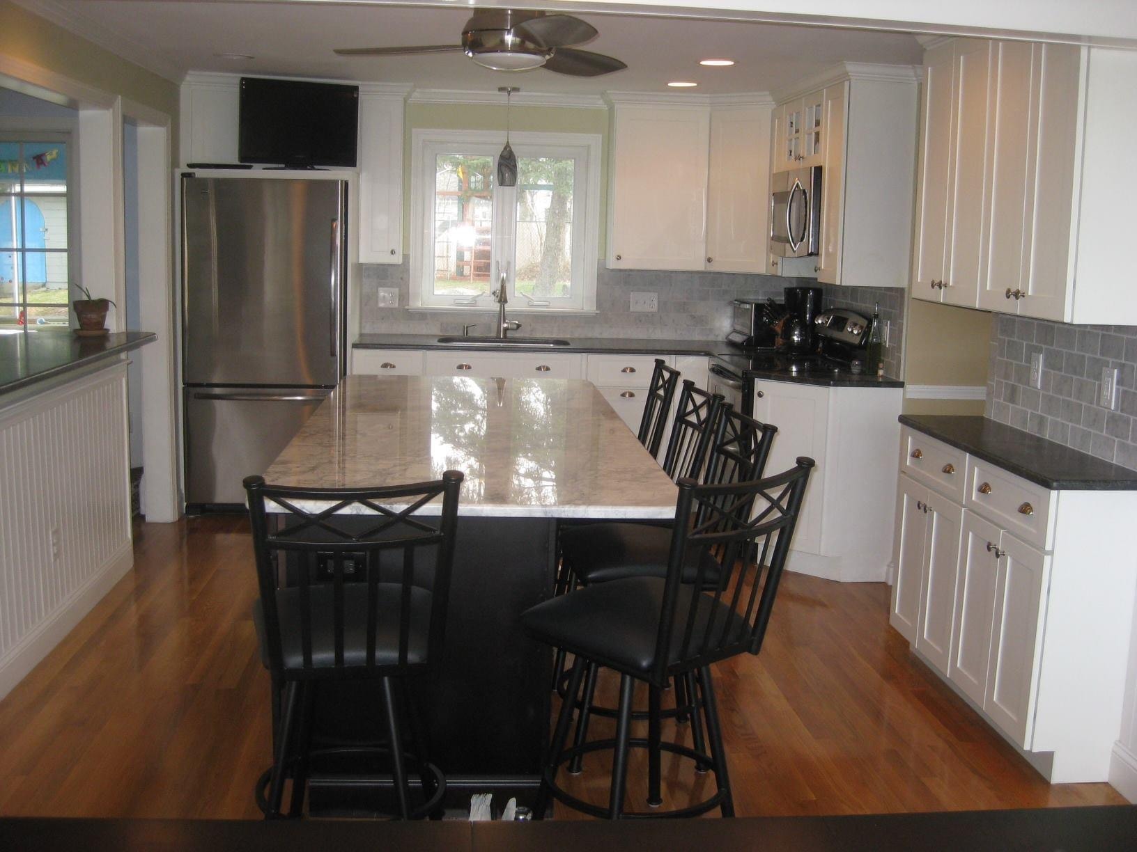 After photo of a remodeled open kitchen with white cabinetry, large center island, stone countertop, stainless-steel appliances and hardwood flooring by Boston J's Roofing and Construction