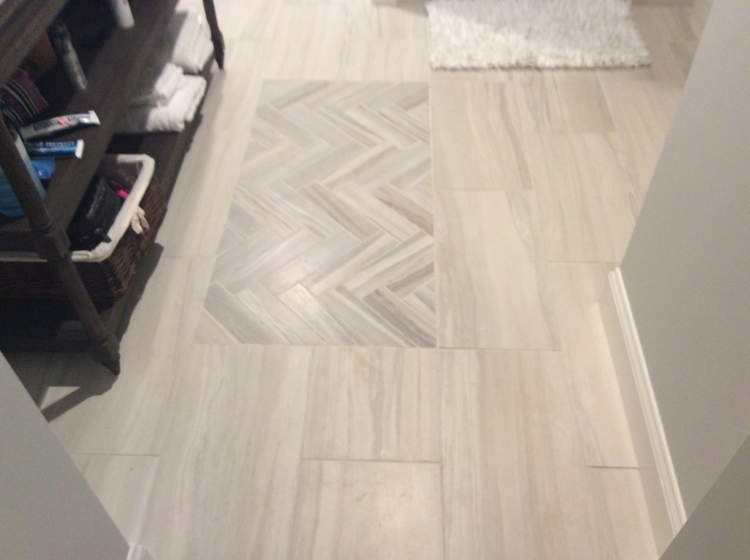 Custom floor tile inlay by Boston J's featuring a centered herringbone pattern with contrasting border set within light field tile