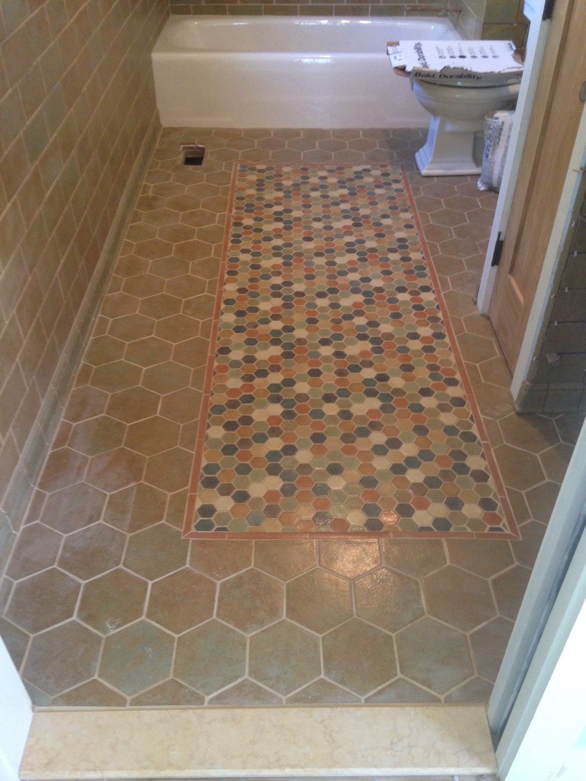 Custom bathroom floor tile inlay by Boston J's featuring a multicolored hexagon mosaic centerpiece framed by larger hexagonal field tile